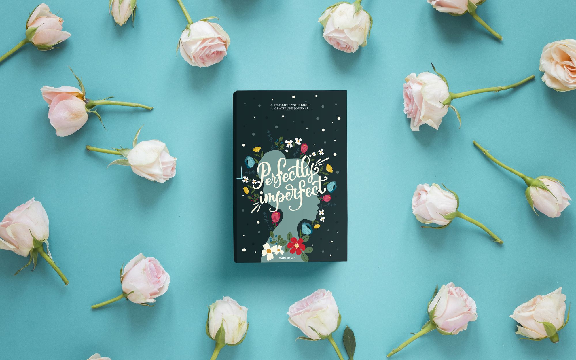 Perfectly Imperfect journal, dark green cover, among pale roses on turquoise