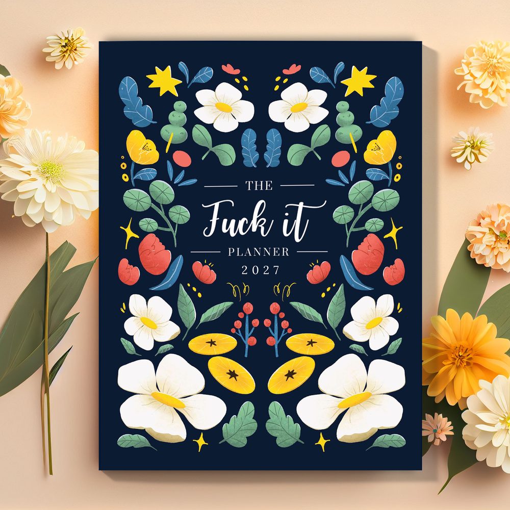 The Fuck It Planner, navy cover with white and yellow flowers, on a peach background with dahlias