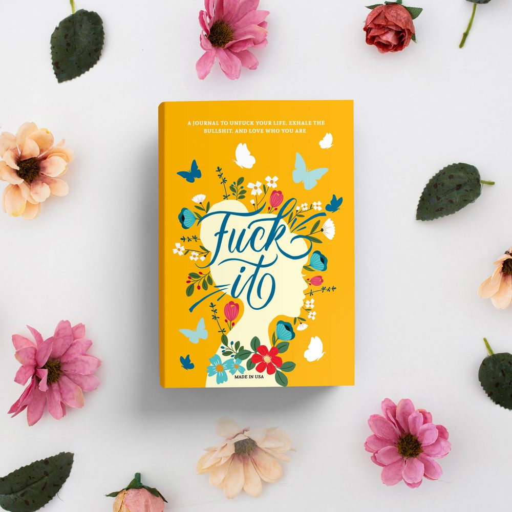 Fuck It journal, yellow cover with blue lettering and butterflies, among pink flowers on a white background